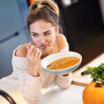 Picture of young woman tasting pumpkin soup in the kitchen.