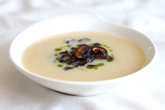 White bowl of creamy garlic soup with mushrooms and green chive oil on top.