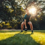 Full length portrait of fit young man training with kettlebell in the park.