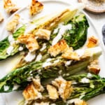 Grilled romaine lettuce with croutons and drizzled dressing on a plate.